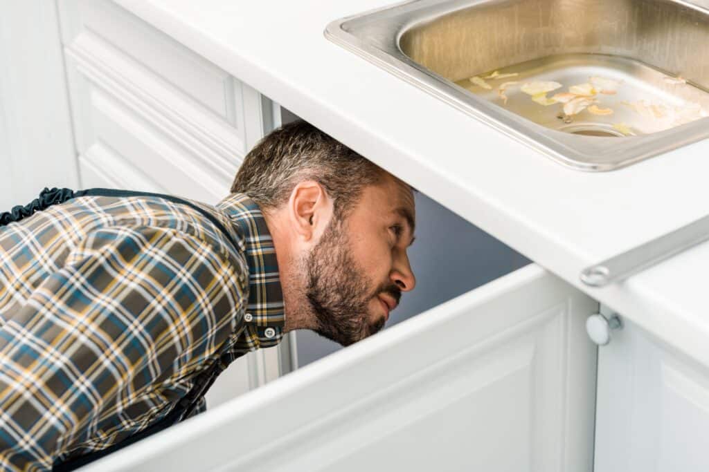 plumber looking under broken sink in kitchen