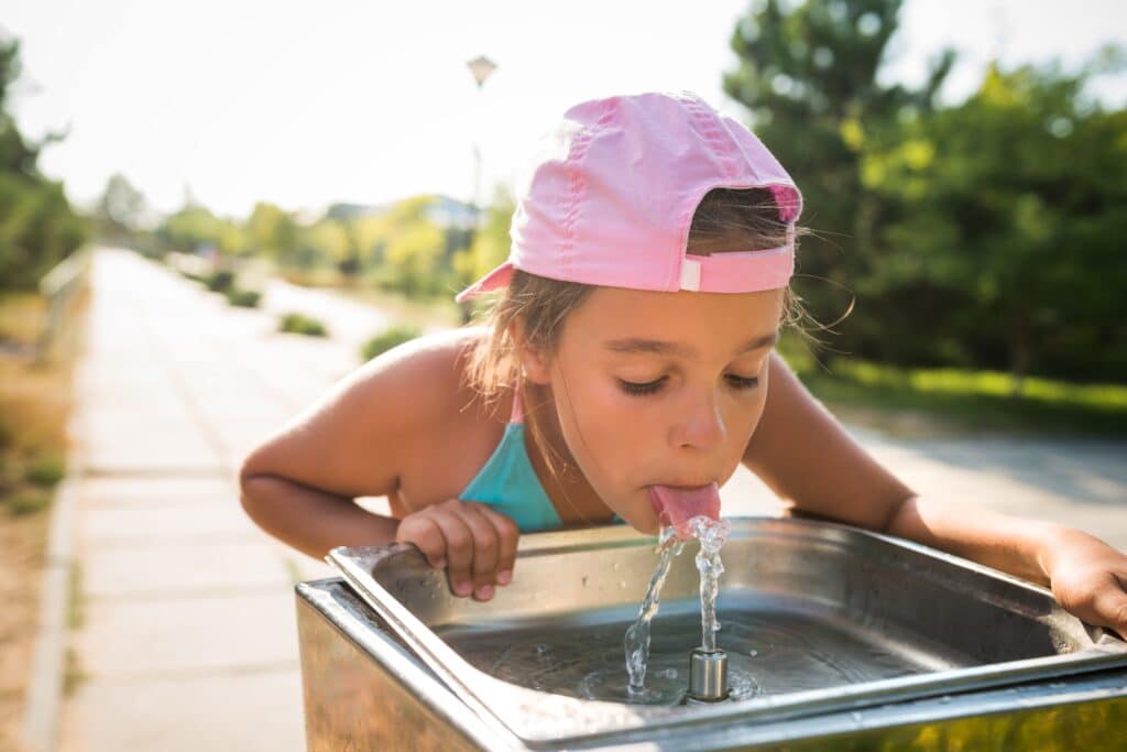 Cute thirsty girl drinks water from drinking sink